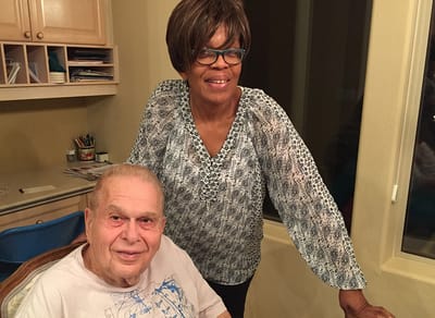 A caregiver standing next to a senior in an indoor setting.