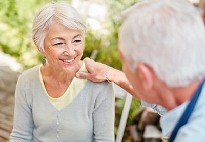 A senior woman smiling with a caregiver outdoors.