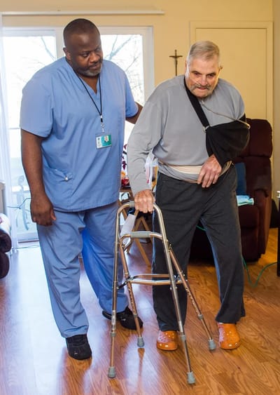 Staff assisting a resident with a walker indoors.