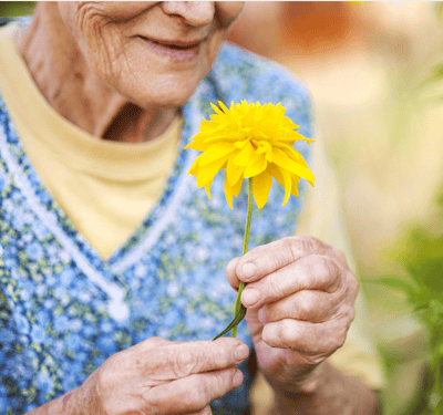 Elderly woman holding a yellow flower outdoors