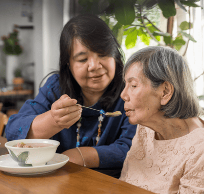 Caregiver feeding a senior resident in a warm setting.