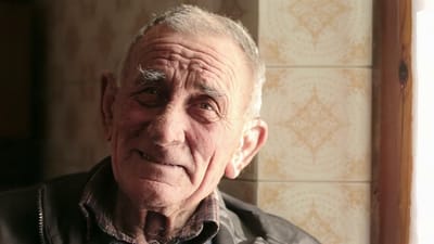 A smiling elderly man in a cozy interior setting.