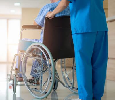Staff assisting a resident in a wheelchair indoors.
