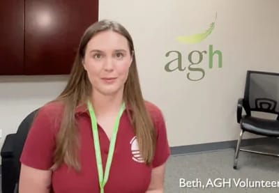 AGH Volunteer standing in front of facility logo.