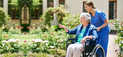 A caregiver pushing a resident in a wheelchair through a garden