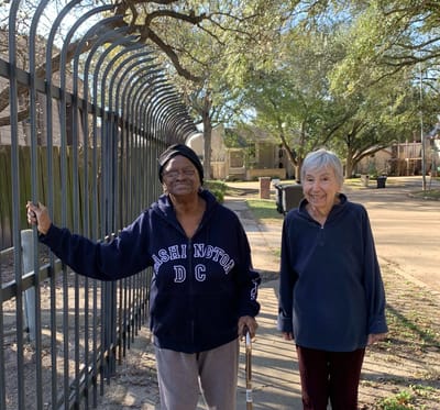 Two elderly women smiling by a decorative fence outside