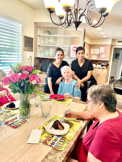 Residents enjoying cake with staff in dining area.