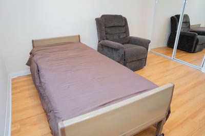 Simple private resident room with a bed and chair.