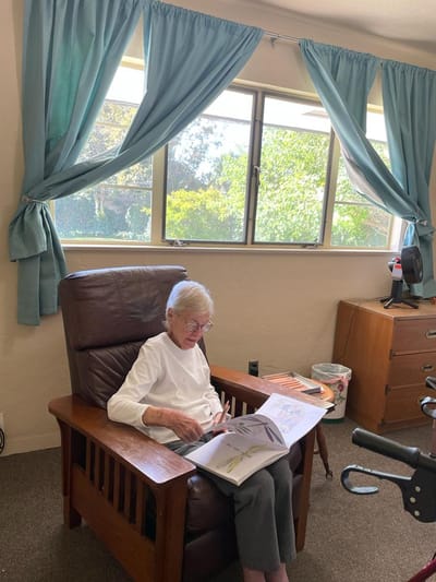 Senior resident reading in a cozy chair by the window.