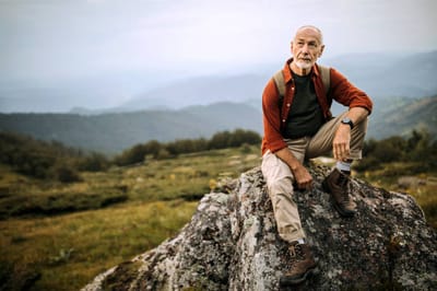 An older man sitting on a rock in a natural outdoor setting