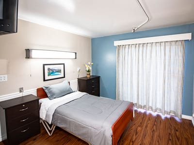 Brightly lit private resident room with bed and window.