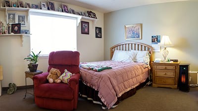 Cozy resident room with bed, chair, and personal photos