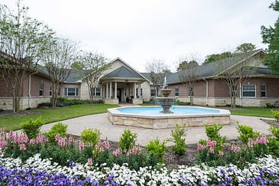 Exterior view of a senior living facility with a fountain and gardens