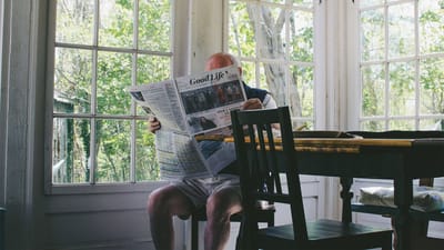 Senior man reading a newspaper indoors by a window