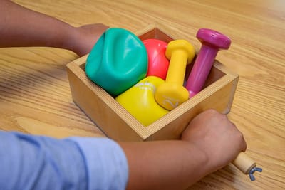 Hands holding a wooden box of colorful exercise equipment