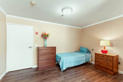 Private room with a bed, dresser, and lamp