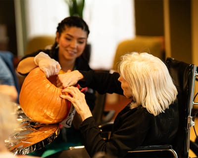 Resident and staff member carving a pumpkin together