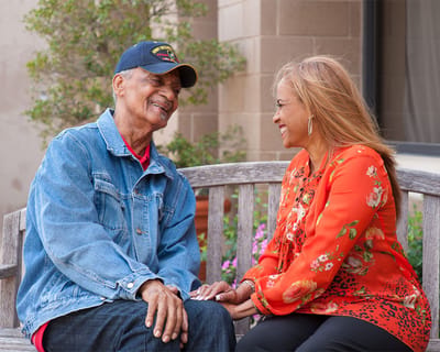 Two residents smiling and holding hands on a bench