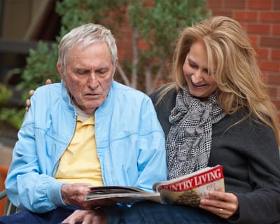 A resident and staff member reading together outdoors