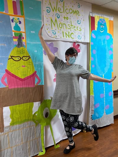 Staff member posing next to a colorful backdrop from a themed event