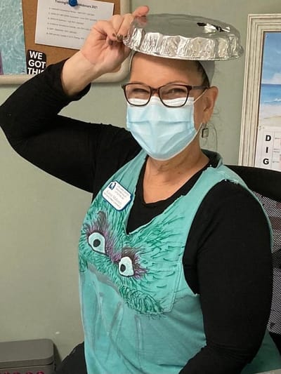 Staff member wearing a foil hat and mask, smiling