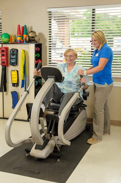 A resident using a fitness machine with staff assistance