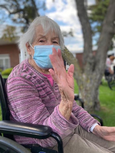 Resident waving outdoors with a mask on