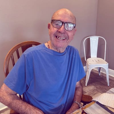 A smiling senior man sitting in a chair inside