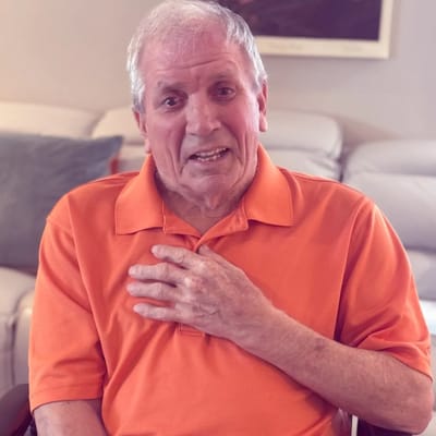 A senior man in an orange polo shirt, engaging with the camera