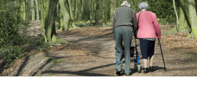 Two seniors walking in a wooded area.