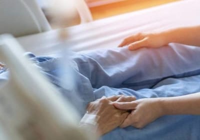 Caregiver holding a patient's hand in a bed
