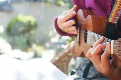 Close-up of hands playing a guitar outdoors.
