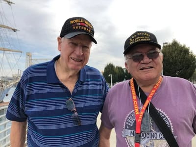 Two elderly veterans posing outdoors with hats