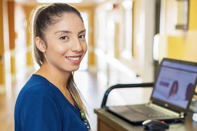 Nurse smiling at a laptop in the facility hallway