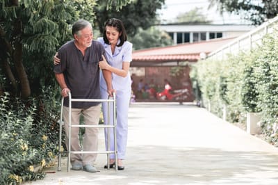 Nurse assisting a resident with a walker outdoors
