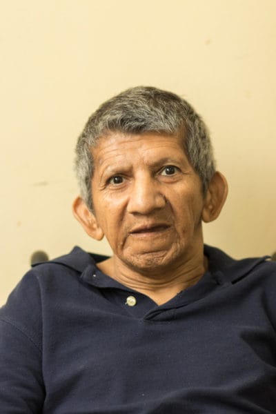 Elderly man sitting indoors, looking at the camera