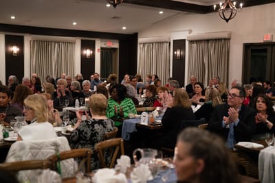 Many people sitting at tables, clapping during an event