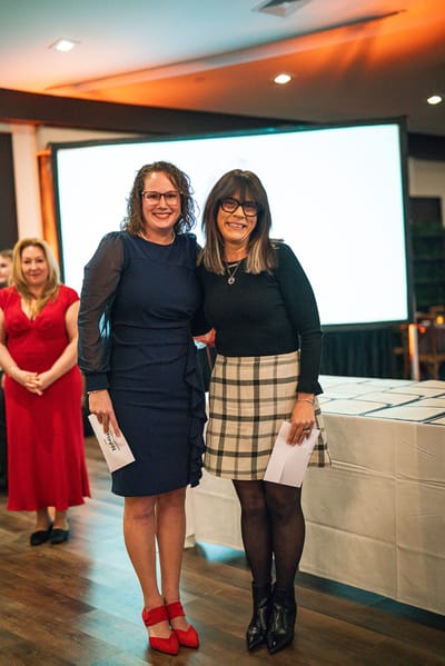 Two women posing with certificates at an awards ceremony