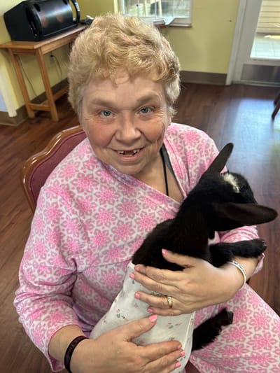 A resident holding a small goat in a cozy interior
