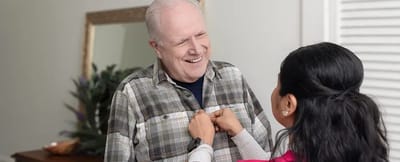 Caregiver assisting a smiling older man indoors
