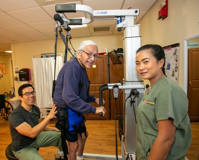 Resident using rehabilitation equipment with staff assistance
