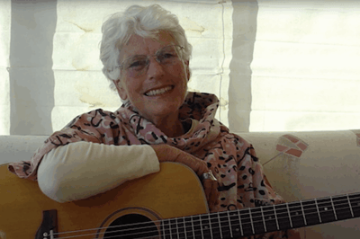 Senior woman playing guitar, smiling warmly.