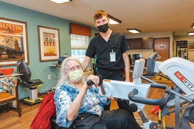 A staff member assists a resident with exercise equipment