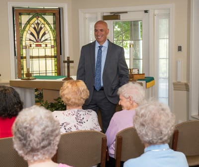 A well-dressed man speaking to residents in a common area