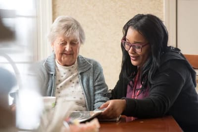 Staff assisting a resident with a book in a cozy interior