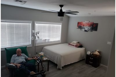 A resident sitting in a private room with a bed and decor