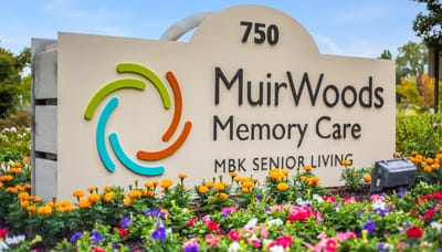 Sign for MuirWoods Memory Care with flowers in front