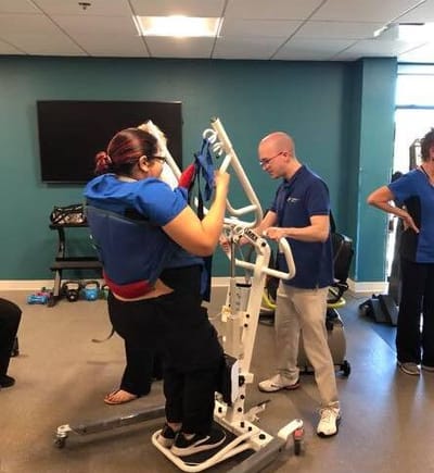 Staff assisting a resident with a lift device in a therapy room