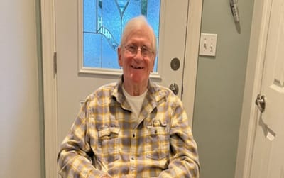 A smiling senior man in a checkered shirt sitting indoors