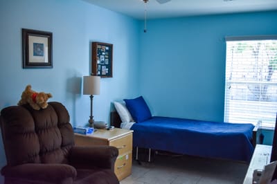 A cozy resident room with blue walls and a chair